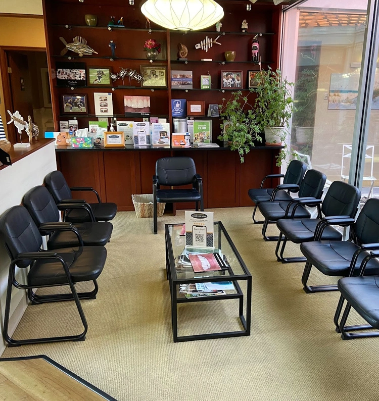 Modern dental office waiting room with black chairs, display shelves, and glass table with reading materials.