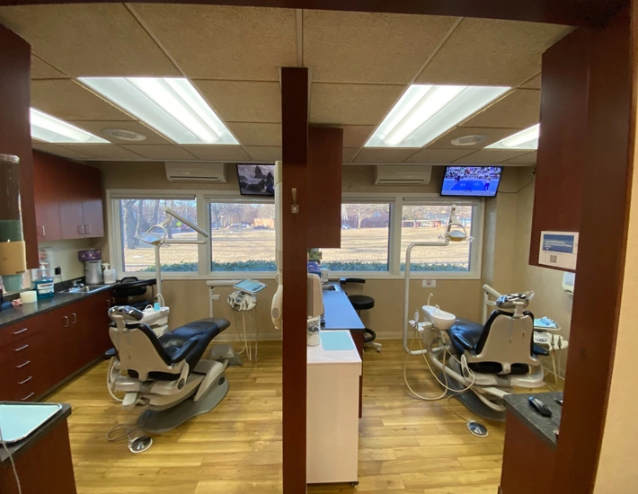 Modern dental operatory with two patient chairs, equipment, and large windows overlooking outdoor landscape.