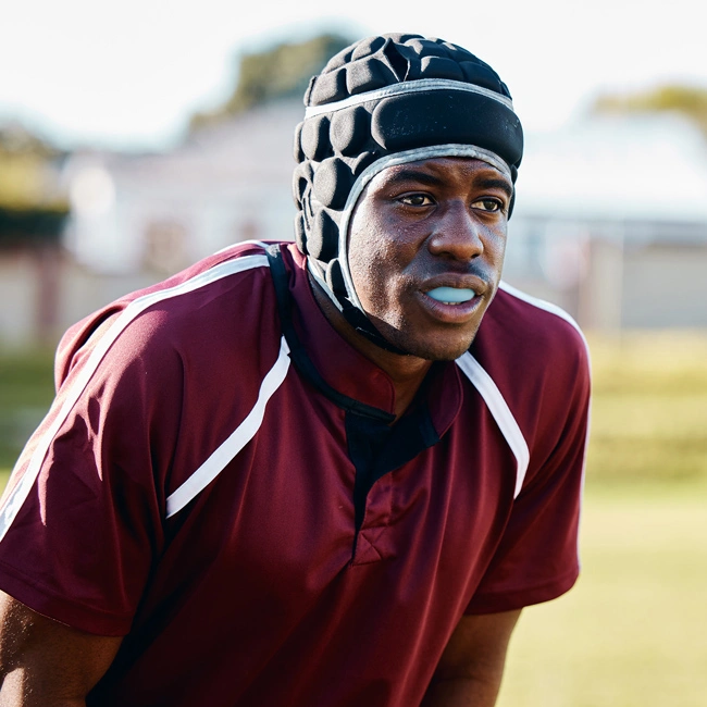 Male athlete wearing maroon jersey and protective headgear on outdoor field.
