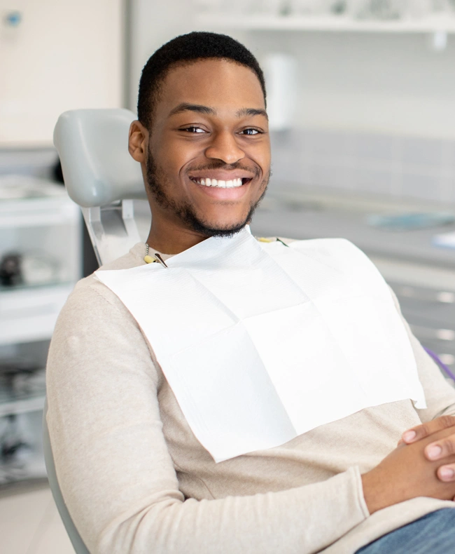 Smiling male patient wearing dental bib seated in dentist chair at dental office.