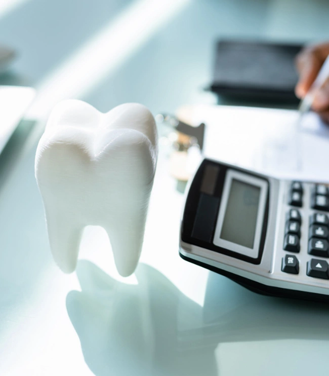 White tooth model beside calculator on dental office desk during cost consultation.