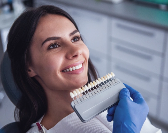 Woman smiling while holding dental shade guide in professional dental office setting.