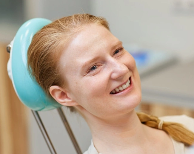 Young patient smiling in dental chair with blue headrest at family dental office.