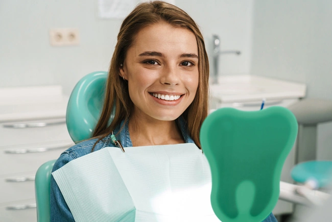 Happy young woman sitting in dental chair holding paperwork in modern dental office