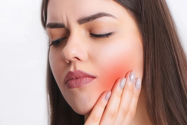 Woman experiencing jaw pain, holding cheek with red inflammation highlighted against white background.