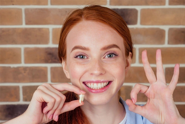 Young woman with red hair smiling at camera while holding dental floss against brick wall background.