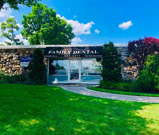 Gold Coast Family Dental storefront with glass doors, stone exterior, manicured lawn, and landscaping under blue sky.