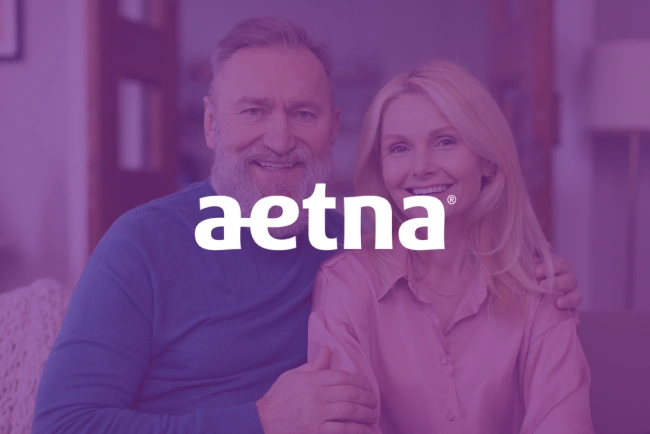Smiling couple in casual clothing indoors with Aetna logo overlay in purple tones.