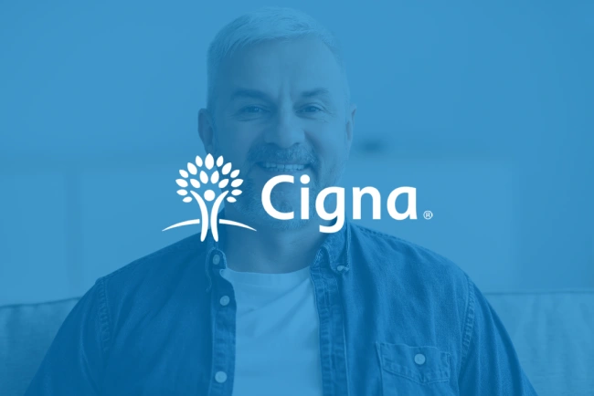 Cigna logo overlaid on smiling man in blue shirt against blue background.