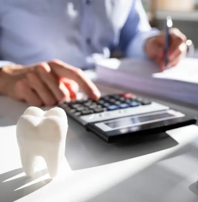 Dentist calculating dental membership costs using calculator and reviewing treatment plan.